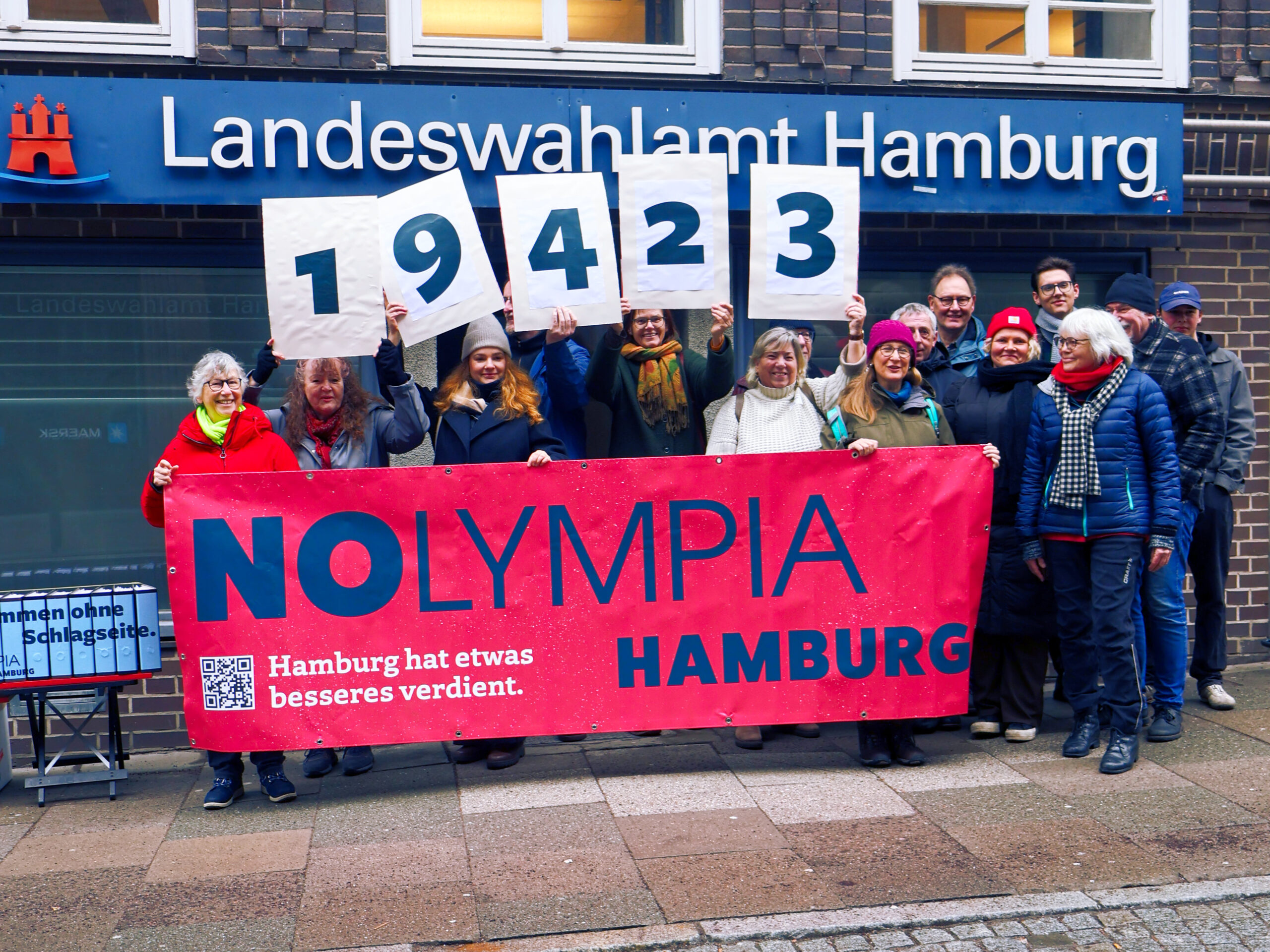 Aktive von NOlympia Hamburg stehen vor dem Landeswahlamt. Sie halten Schilder mit der Zahl 19.423 – die Anzahl der Unterschriften, die am 21.02.2026 dem Landeswahlleiter übergeben wurden.
